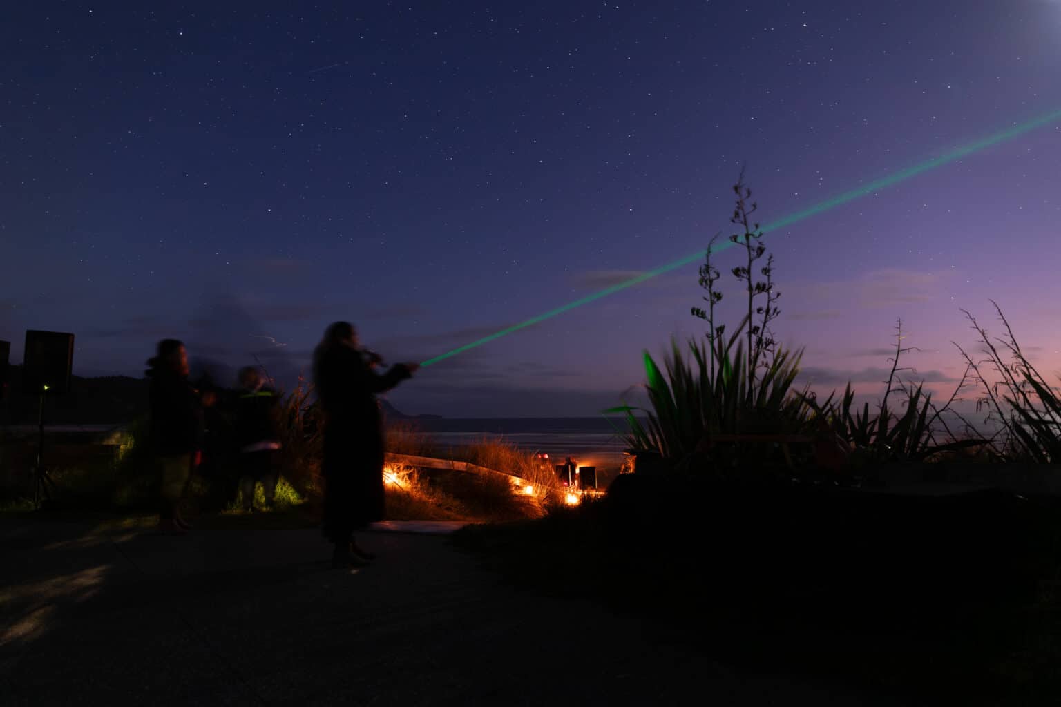 A woman holding a lazer light points it towards a starry sky