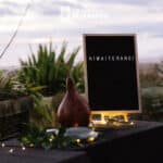 A view of a decorative table looking out over an ocean There is a gourd, a letterboard sign that says Hiwaiterangi and fairy lights on the table