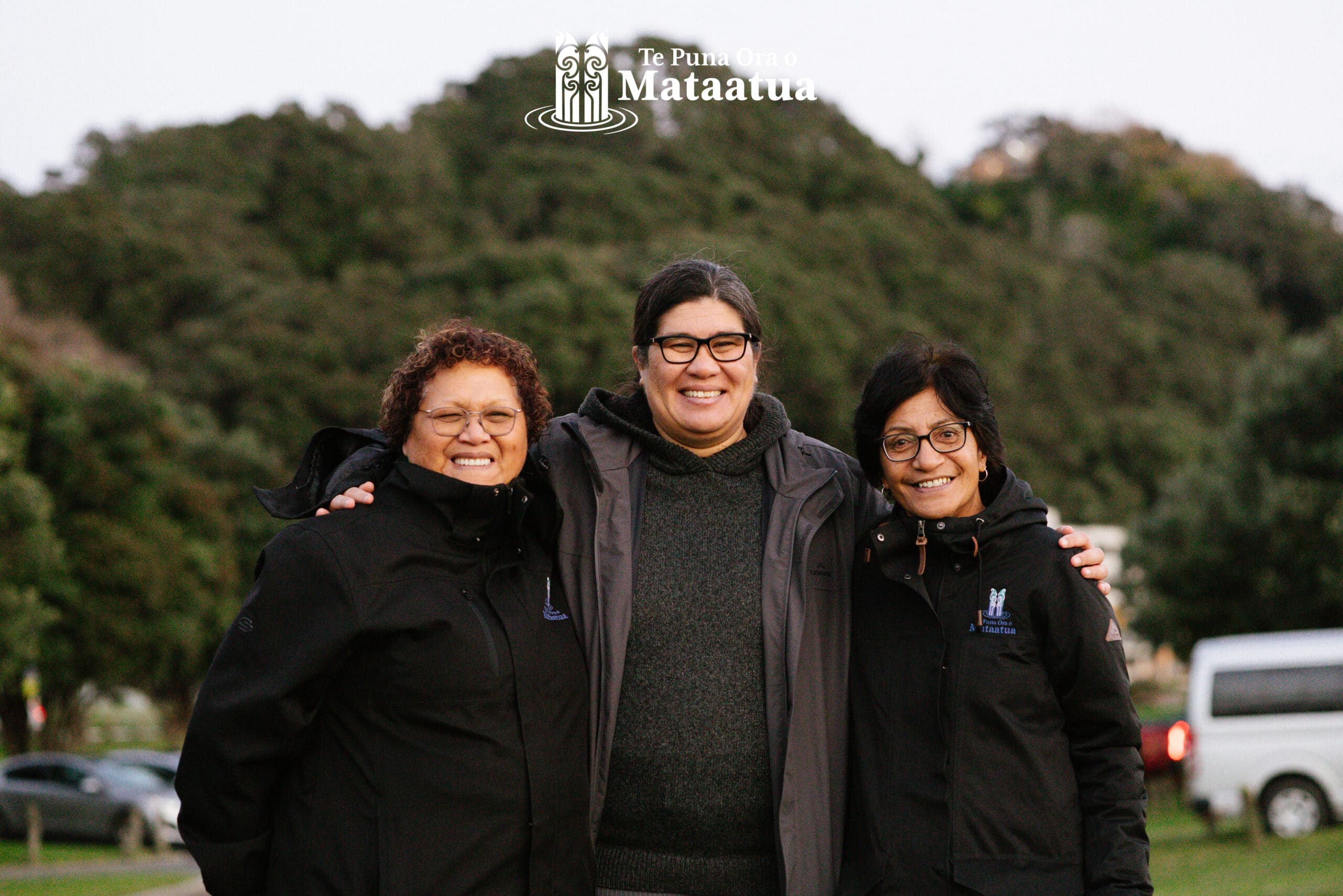 A group of people stand smiling against a backdrop of native bush