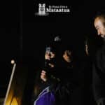 A group of children watch on as a small girl dressed in black and purple gives a karakia/prayer