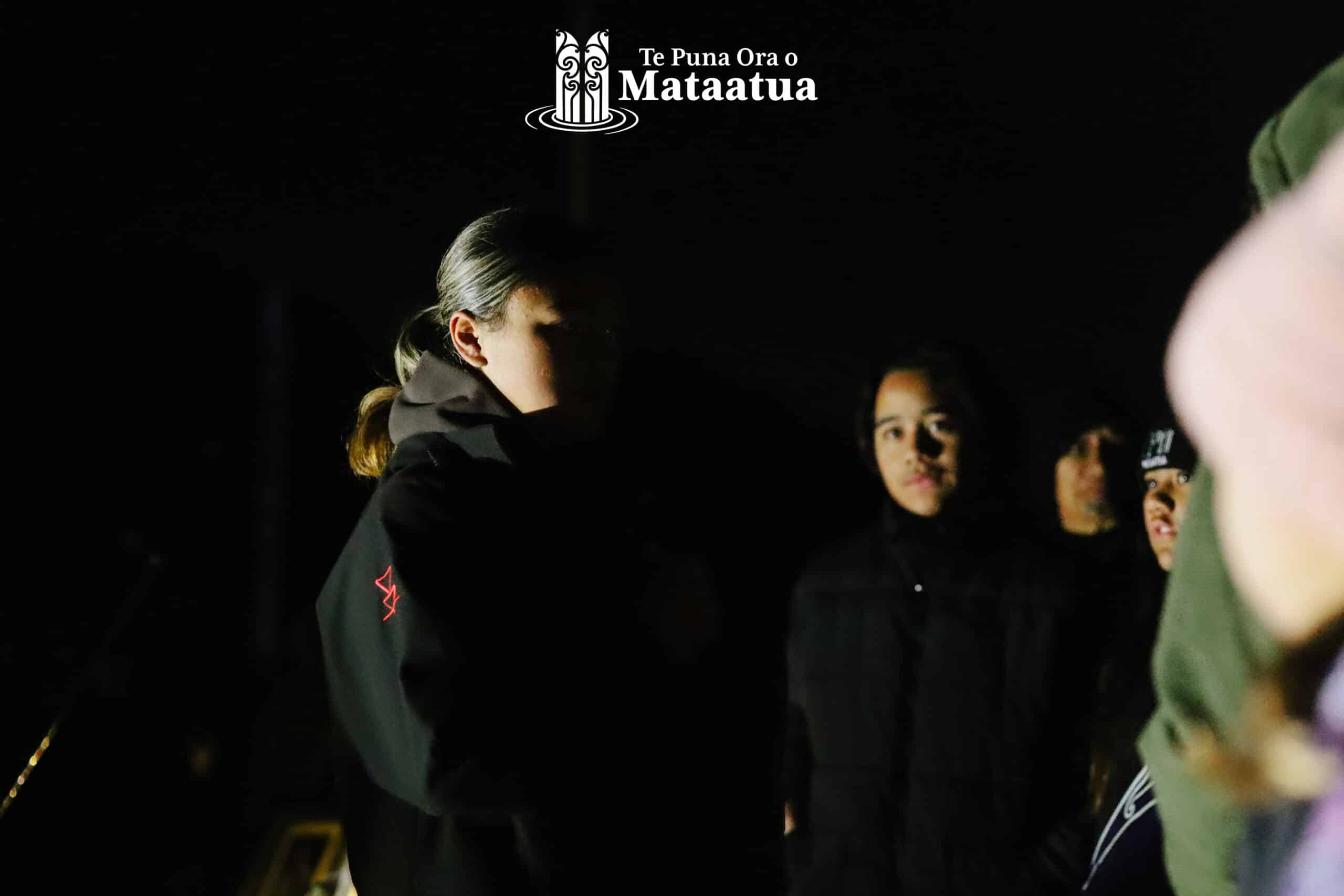 A group of children watch on as a small girl dressed in black gives a karakia/prayer