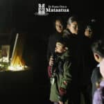 A group of children watch on as a small boy dressed in green gives a karakia/prayer