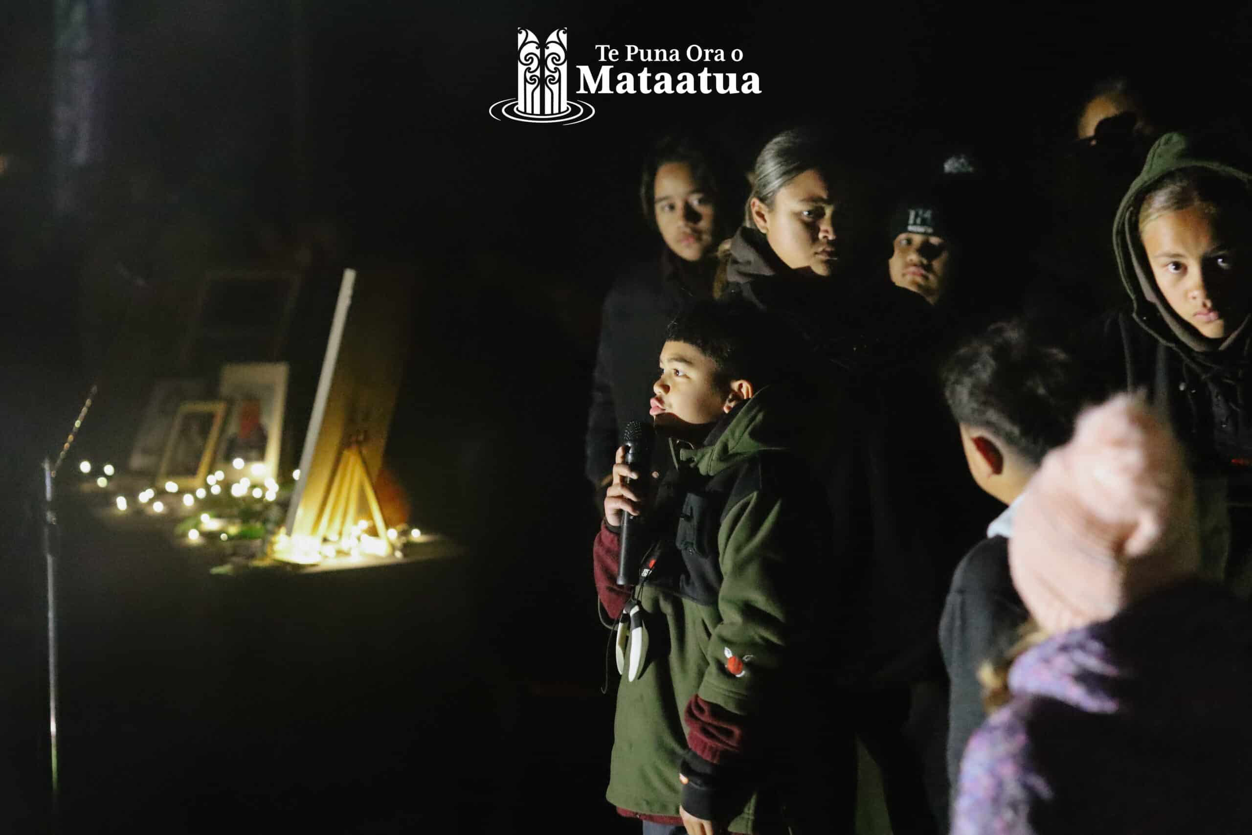 A group of children watch on as a small boy dressed in green gives a karakia/prayer