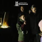 A group of children watch on as a small boy dressed in green gives a karakia/prayer