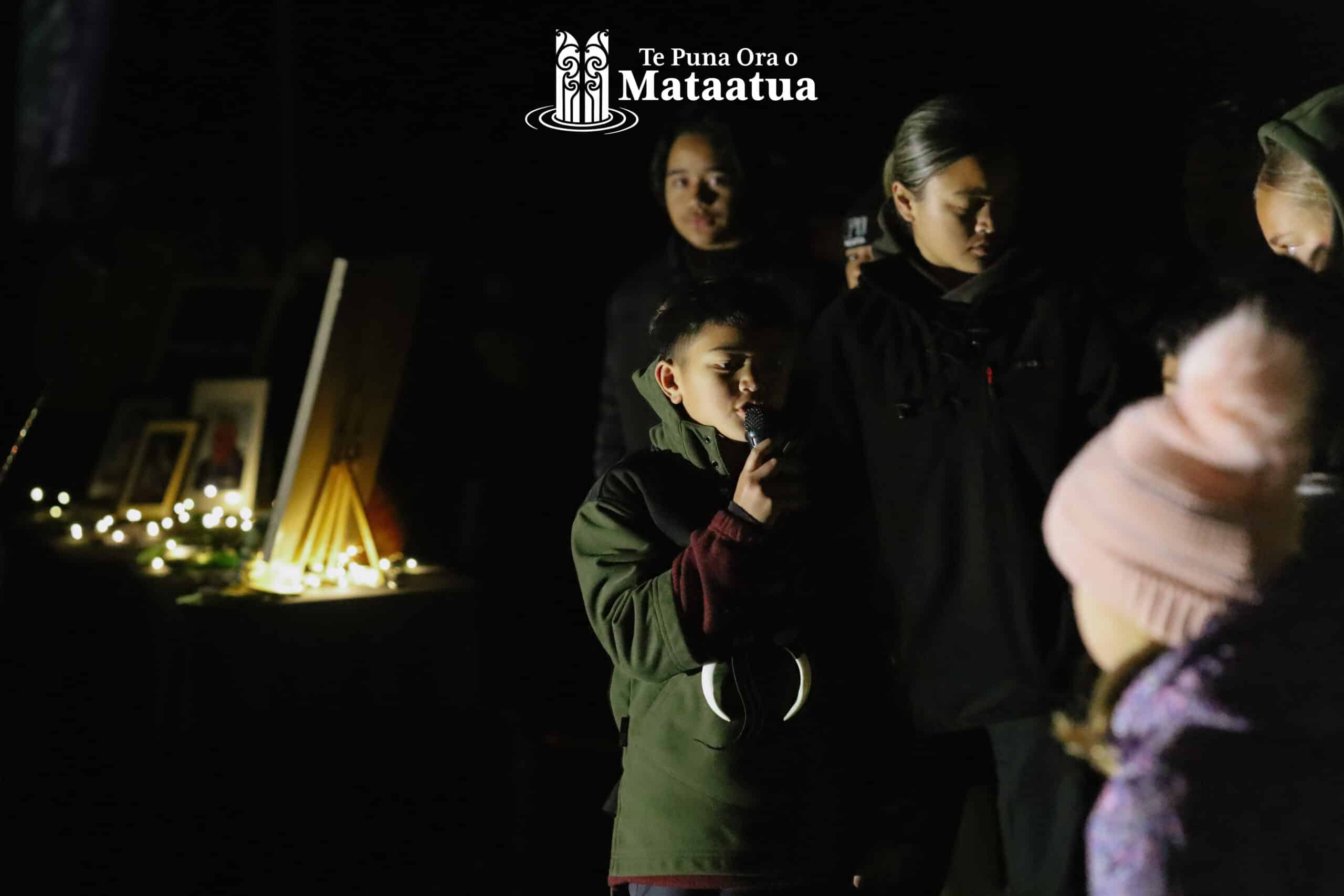 A group of children watch on as a small boy dressed in green gives a karakia/prayer