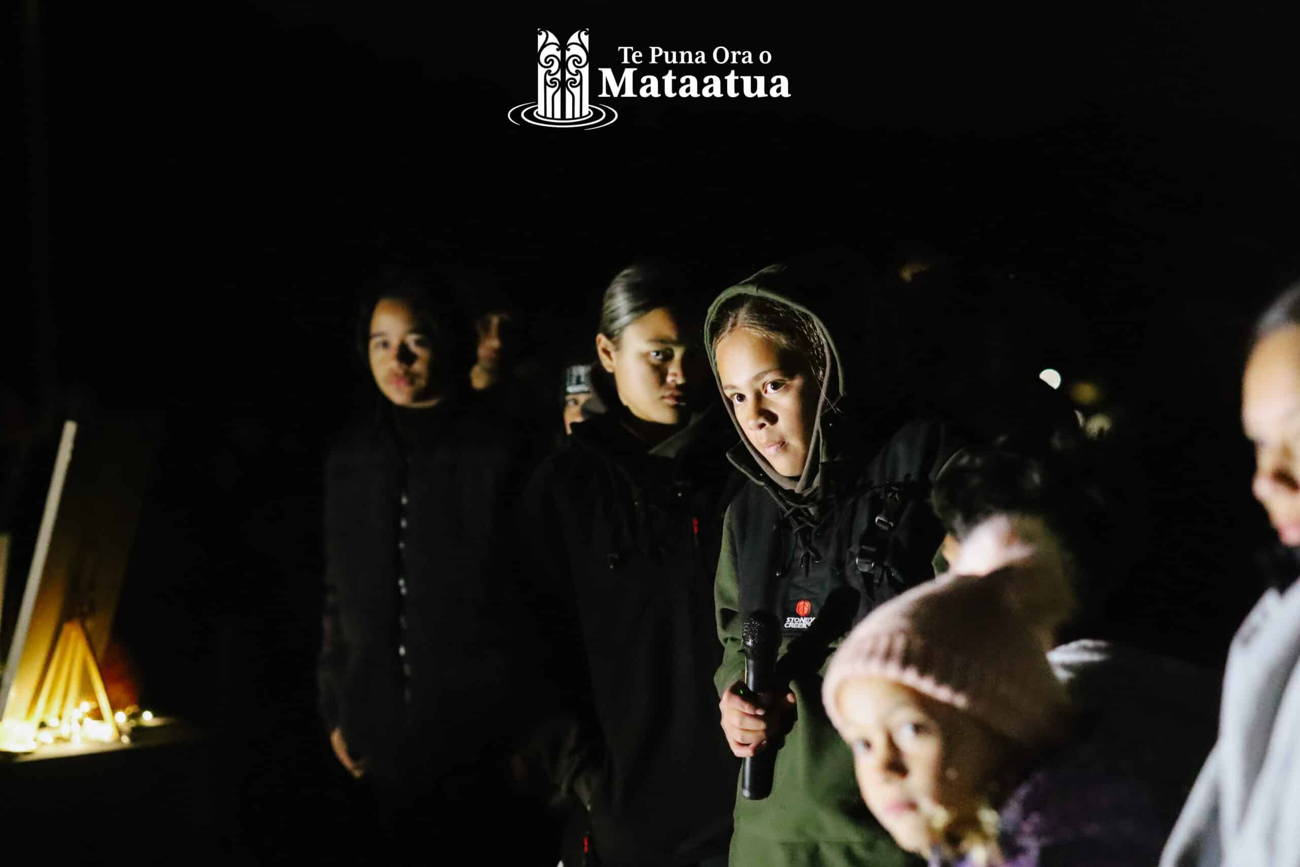 A group of children watch on as a small girl dressed in green gives a karakia/prayer