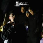 A group of children watch on as a small boy dressed in black gives a karakia/prayer