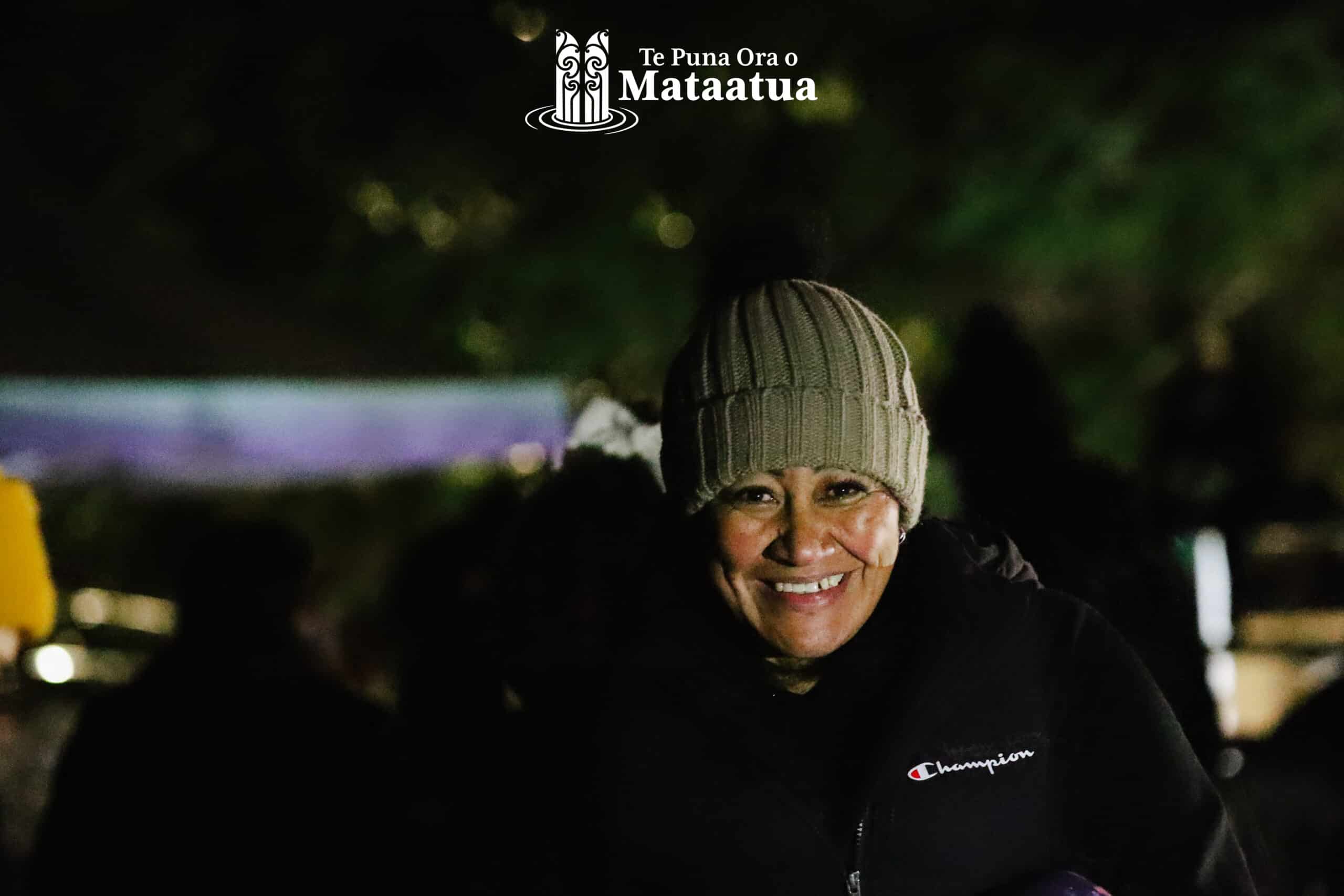 A woman in a green beanie smiles. Image taken in the dark light of dawn