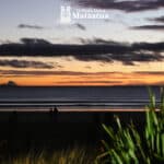 A cloudy sunrise looking over the horizon of a still ocean, Ōhope beach. On the horizon Whakaari White Island has a small plume of steam