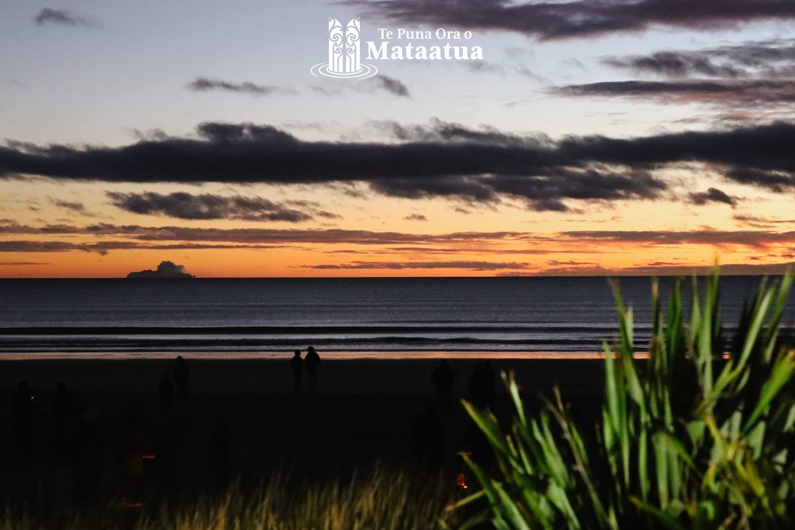 A cloudy sunrise looking over the horizon of a still ocean, Ōhope beach. On the horizon Whakaari White Island has a small plume of steam