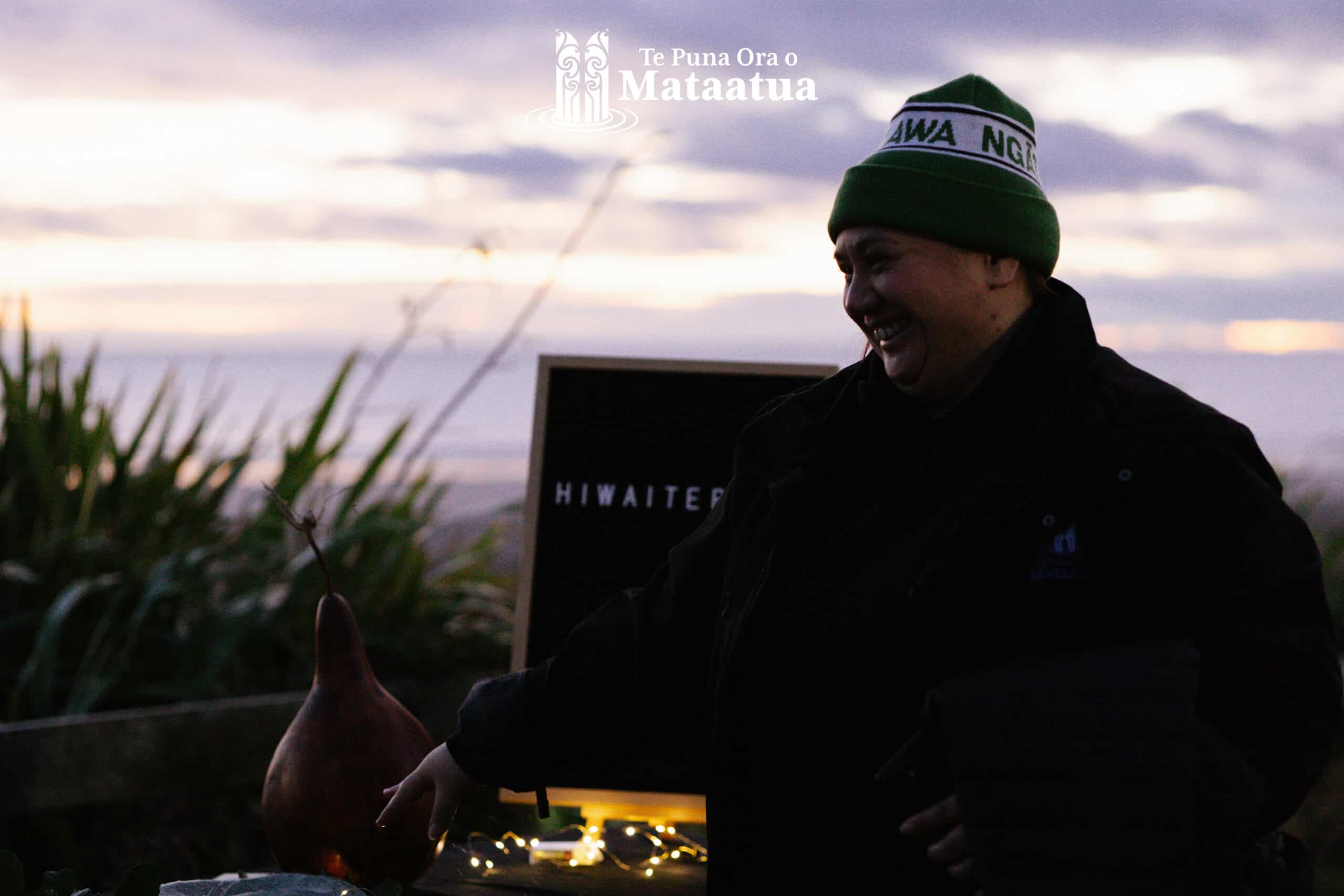 A woman smiles engaging with a decorative Matariki display that has a gourd and fairy lights on it