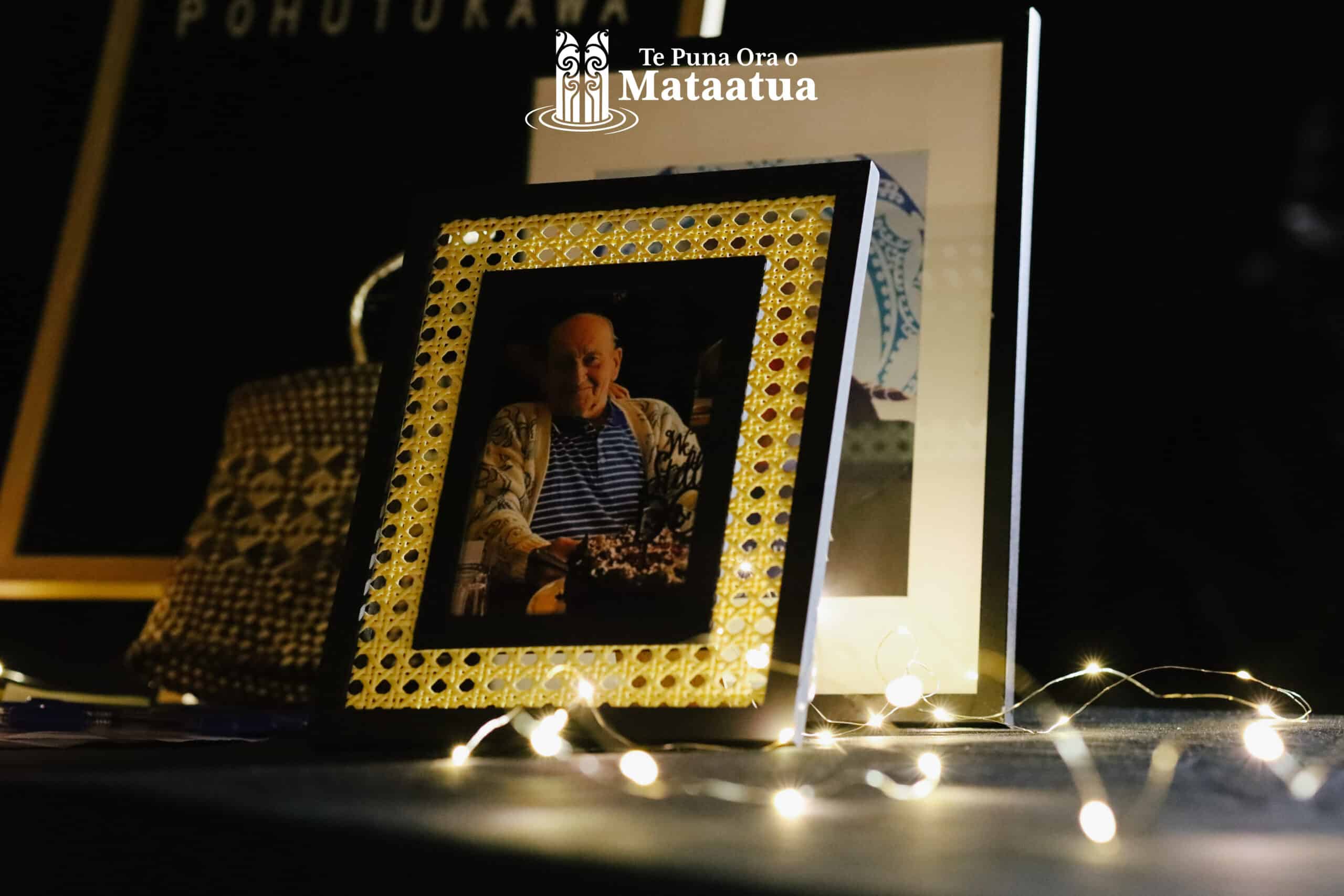 A photo of an elderly man is lightly lit by fairy lights